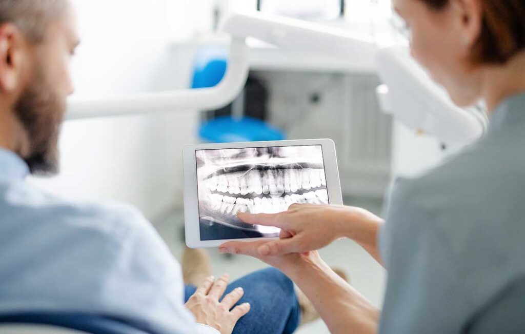 Adult examining stained teeth in a bathroom mirror beside a toothbrush and dental floss.
