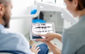 Adult examining stained teeth in a bathroom mirror beside a toothbrush and dental floss.
