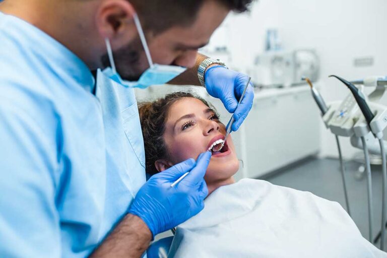 Person gently brushing along the gumline beside a mirror with floss and toothpaste nearby.